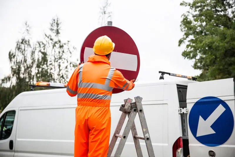 Medewerker in oranje pak plaatst een verkeersbord bij een bus