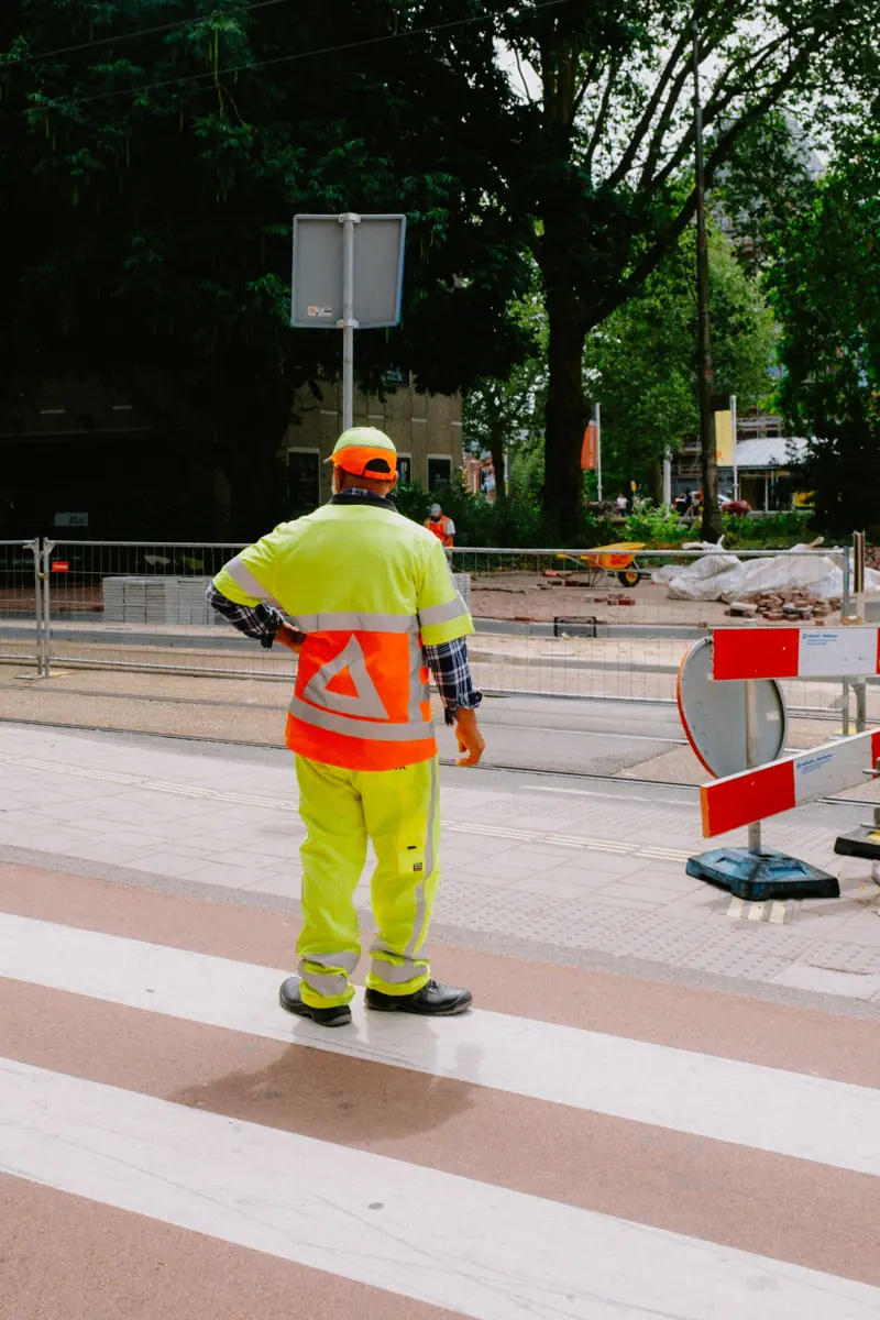 Verkeersregelaar in hesje bij een zebrapad naast een afgezette bouwplaats